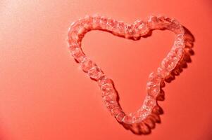 Close up of invisible aligners on pink background with copy space. Plastic braces dental retainers for teeth straightening photo