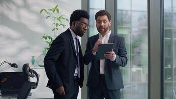 Two diversity multiethnic business men colleagues discuss online success looking in digital tablet computer amazed with good news multiracial businessmen males talking in office about startup growth video