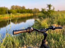 Bicycle handlebar overlooking tranquil river during sunset, inviting exploration of nature photo