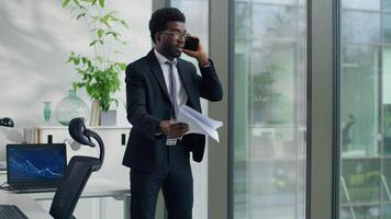 African American ethnic business man angry arguing with mobile phone call problem holding papers in office furious businessman male yelling with smartphone throwing documents away looking out window video