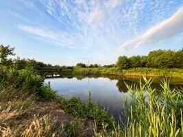 Small wooden bridge crossing calm river at sunset with cloudy sky. photo