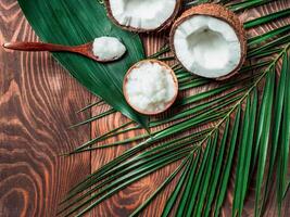 Top view of coconut MCT oil in bowl and in spoon and halved coco-nut on wooden table. Health Benefits of MCT Oil. MCT or medium-chain triglycerides, form of saturated fatty acid. Flat lay. Copy space photo