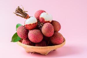 Juicy Lychee with cut in half and leaves on bamboo basket isolated on pink background. Thai fruits photo