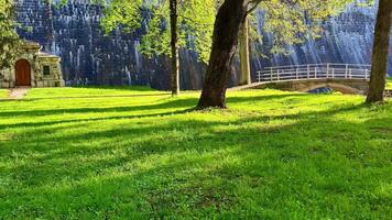 Explore a tranquil park featuring a stunning waterfall, lush greenery, and a quaint building among towering trees, ideal for relaxation video