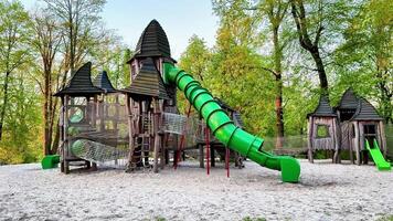This highlights a lively playground with a large green slide at its center, where children play and interact with equipment, while a charming castle adds a whimsical touch video