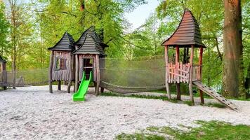 Discover a delightful wooden playground in a lively park, with a green slide for adventures, a cozy hammock, and a charming playhouse for family fun video
