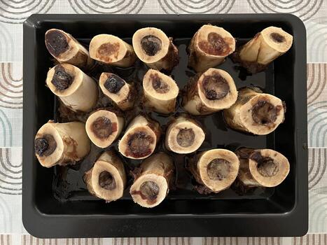 Roasted homemade bone marrow in a cooking tray, oven-cooked and served on a patterned tablecloth. The rich, roasted texture of the marrow contrasts with the casual and cozy table setting photo