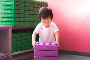 Baby boy is happily playing with purple blocks, developing fine motor skills, hand and finger muscles, imagination and creativity with toys. 2 year old child. photo