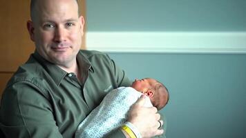 Father tenderly holding newborn baby wrapped in a blanket, symbolizing emotional connection, early bonding, and the intimate joy of parenthood in a peaceful indoor setting. video