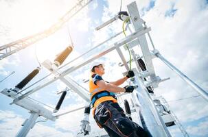 Electrician in protective helmet working on high voltage power lines. Highly skilled workmen servicing the electricity grid. Modern power station photo