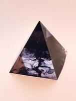 An intriguing eye-level shot captures a polished, dark pyramid with captivating internal swirls and patterns, hinting at a natural stone or resin. The object rests on a soft, light-colored background photo