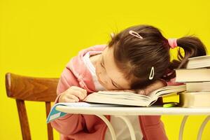 Little school girl sitting at table, tired, put her head on books, expresses fatigue from studying and difficulties in assimilating educational material, is stressed. photo