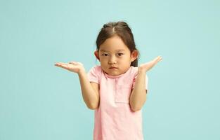 Confused Preschool Chinese Child Girl with Shrugged Shoulders saying I Don't Know, Questioningly and Puzzled, she Raised her Hands up, Showing Uncertainty or Lack of Knowledge, Studio Portrait photo