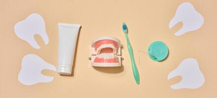 A tube of toothpaste, a toothbrush, dental floss, and decorative elements in the form of paper teeth and a jaw with teeth, located on a beige background. photo