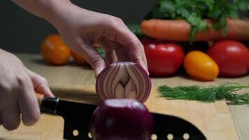 Close-up of hand slicing fresh red onion on wooden cutting board with vibrant vegetables in kitchen setting video