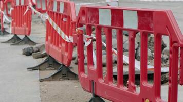 Bright red plastic barriers securing an urban road construction site with caution tape and uneven pavement video