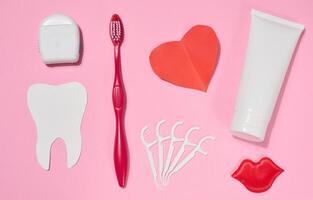 Tube of toothpaste, toothbrush, red paper heart, red decorative lips, dental floss in case and plastic floss holders arranged on pink background. photo