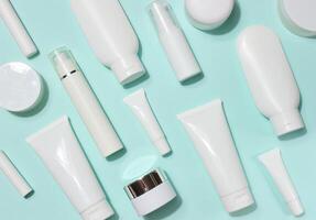 A variety of white plastic tubes and bottles with cosmetics, randomly arranged on a light blue background. Top view photo