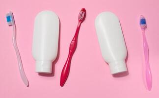 Three toothbrushes and two white plastic tubes of toothpaste placed on a pink background. photo