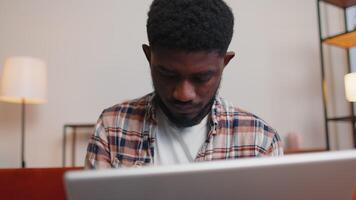 Excited happy joyful guy use laptop pc typing browsing say Wow yes found out great big win news doing winner gesture. African american man working on computer at home office in living room on sofa video