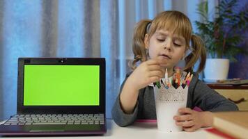 menina comovente lápis fazendo escola programa conectados trabalho de casa, usando computador portátil com verde tela. conectados Aprendendo distância Educação, lição às lar, tecnologia para crianças. Educação durante coronavírus bloqueio video