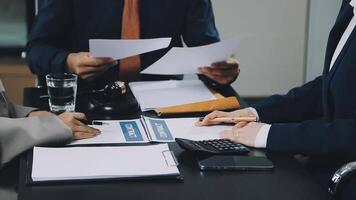 Three business people at a table with papers and a calculator video