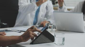 A group of doctors are sitting around a table with a tablet computer video