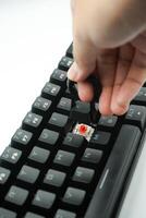 A hand removing keycaps from a black keyboard with a white background photo