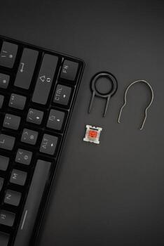 A black mechanical keyboard with a 61 layout with keycaps puller and switch puller and red switches on the side with a black background photo
