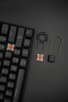 A black mechanical keyboard with a 61 layout with keycaps and switch puller and red switches on the side with a black background photo