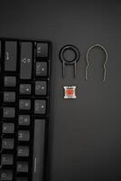 A black mechanical keyboard with a 61 layout with keycaps puller and switch puller and red switches with a black background photo