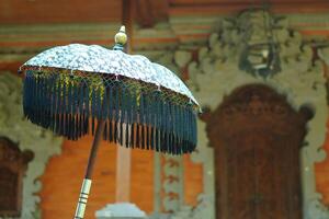 An umbrella made of typical Balinese cloth in front of a building with a typical Balinese style photo