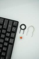 A black mechanical keyboard with keycaps puller and switch puller and red switches on the side with a white background. photo