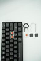 A black mechanical keyboard with a 61 layout with keycaps puller and switch puller and red switches on the side with a white background photo
