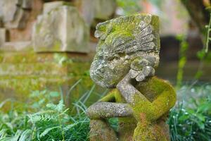 A statue carved from stone posing like a person supporting his chin while sitting with a Balinese concept photo