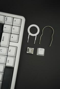 A black and white mechanical keyboard with a monochrome theme with keycaps puller, switch puller, white switches and keycaps with a black background photo