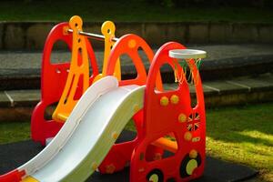 A small children's slide made of plastic with a basketball hoop next to it in a park in the morning photo