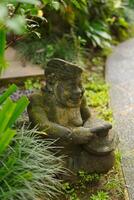 A statue carved from stone with a typical Balinese concept located among the leaves of trees. photo