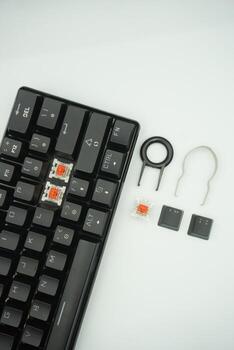A black mechanical keyboard with a 61 layout with keycaps puller and switch puller and red switches on the side in a white background photo