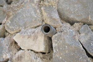 A small pipe in the middle of a wall made of piles of stones in the day photo