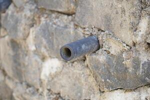 Small pipe in the middle of a wall made of piles of stones photo