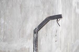 A dirty black pole with exposed wires near a gray wall during the day photo