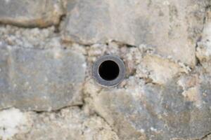 A small pipe in the middle of a wall made of piles of stones photo