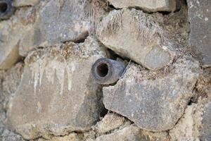 A small pipe in the middle of a wall made of piles of stones with hole photo