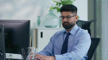 Happy smiling Arabian ethnic Muslim business man Indian businessman typing computer focused with online work looking at camera carefree positive smile male professional guy corporate manager at table video