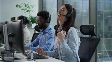 Callcenter success multiethnic operators work computer helpline service agency Caucasian business woman clenching fist successful online trading Indian African coworkers headset call center in office video