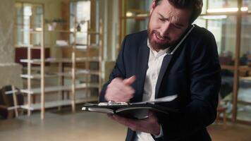 Business angry Caucasian man businessman talk mobile phone multitask arguing in office mad manager worker employee male guy quarrel smartphone overwork problem holding notepad papers documents stress video