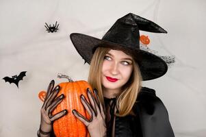 Halloween portrait of beautiful blonde with pumpkin against background with spiderweb with bats and spiders on it. photo