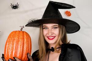 Beautiful woman in witch costume with pumpkin in hands against background with spiderweb. photo