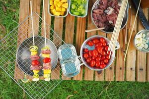 A picnic table with a variety of food, including skewers and tomatoes photo